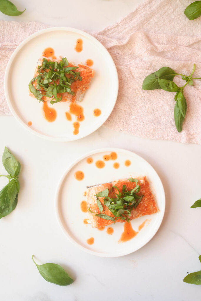 Birds eye view of honey sriracha salmon fillets with basil, plated with basil leaves strewn about