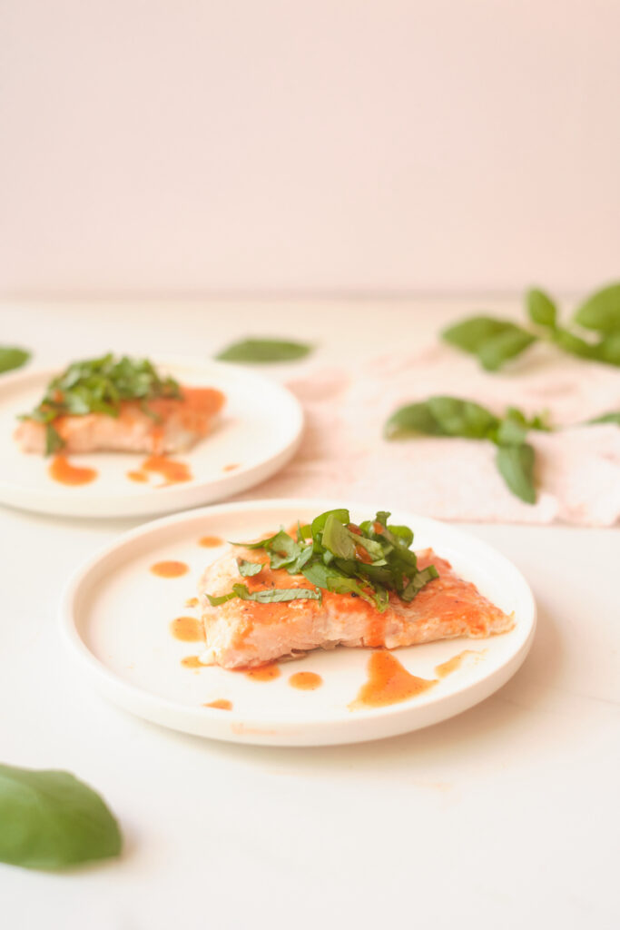 Side view of honey sriracha salmon fillets with basil, plated with basil leaves strewn about