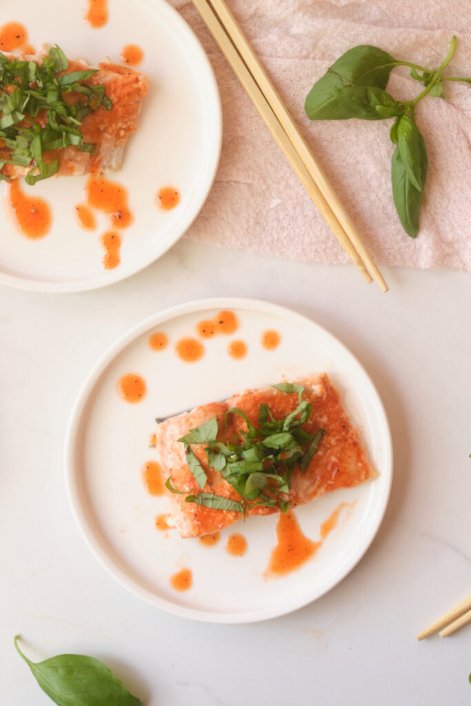 Birds eye view of honey sriracha salmon fillets with basil, plated with basil leaves strewn about and chopsticks in view