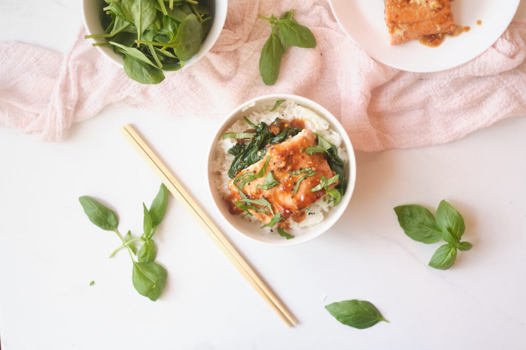 Asian rice bowl with sesame salmon, basil and spinach over rice with some of the ingredients nearby including basil, salmon and spinach