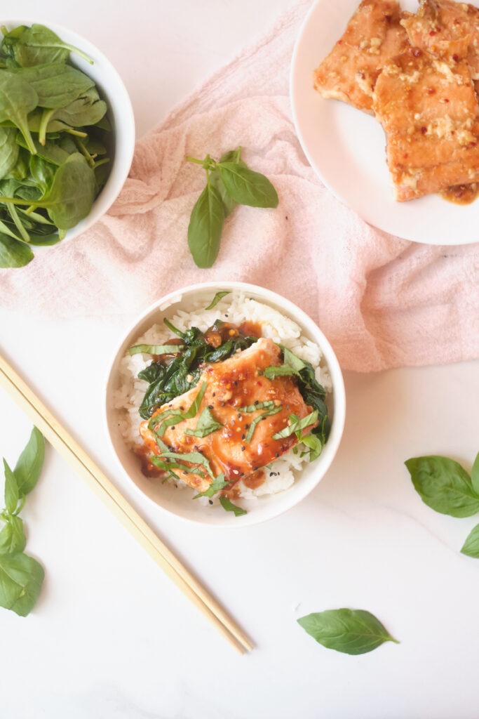 Asian rice bowl with sesame salmon, basil and spinach over rice with some of the ingredients nearby including basil, salmon and spinach