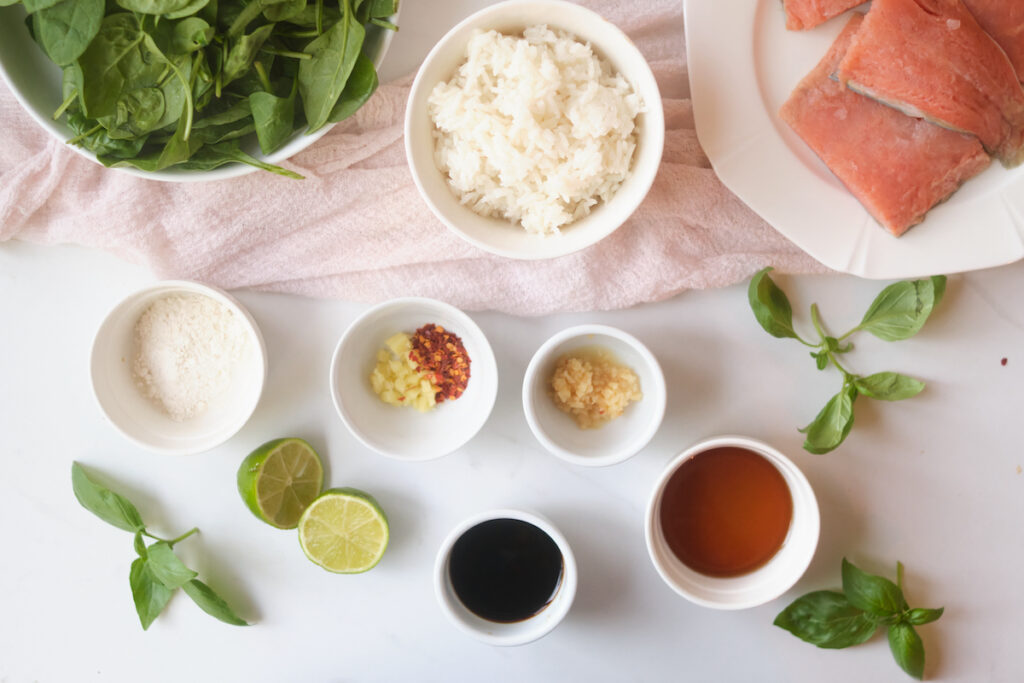 Ingredients for an asian rice bowl recipe including spinach, rice, salmon, and various ingredients for a sauce