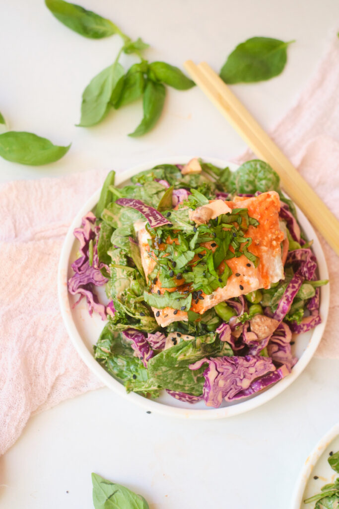 A fillet of salmon piled with fresh basil sits atop an asian sesame salad with fresh veggies