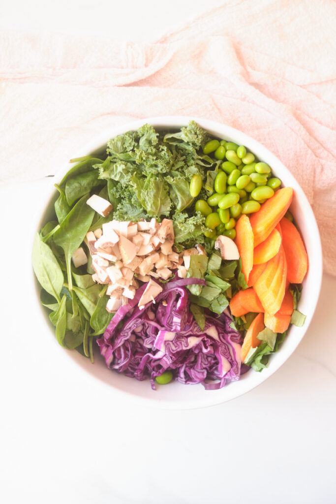 Ingredients for an asian sesame salad with cabbage, basil, spinach, salmon, edamame, kale, and mushrooms in a bowl