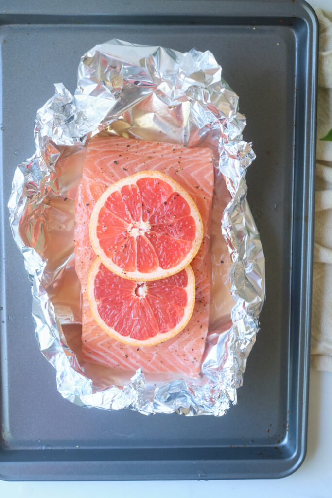 salmon fillet on a tin foil sheet and baking tray before baking and topped with grapefruit slices