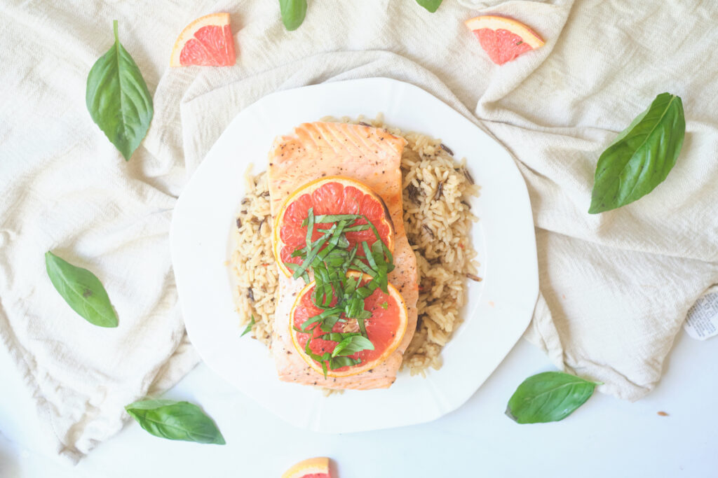 baked grapefruit salmon with grapefruit slices and basil chiffonade on a plate over brown rice with basil and grapefruit triangles strewn about