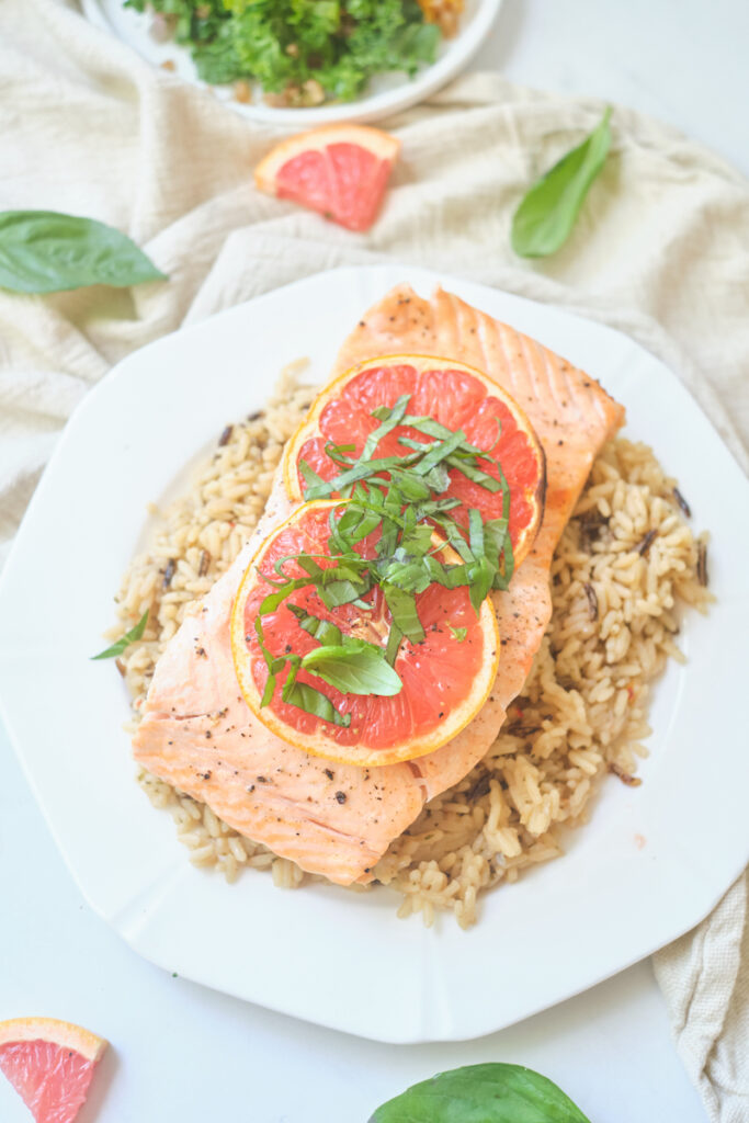 baked grapefruit salmon with grapefruit slices and basil chiffonade on a plate over brown rice with basil and grapefruit triangles strewn about