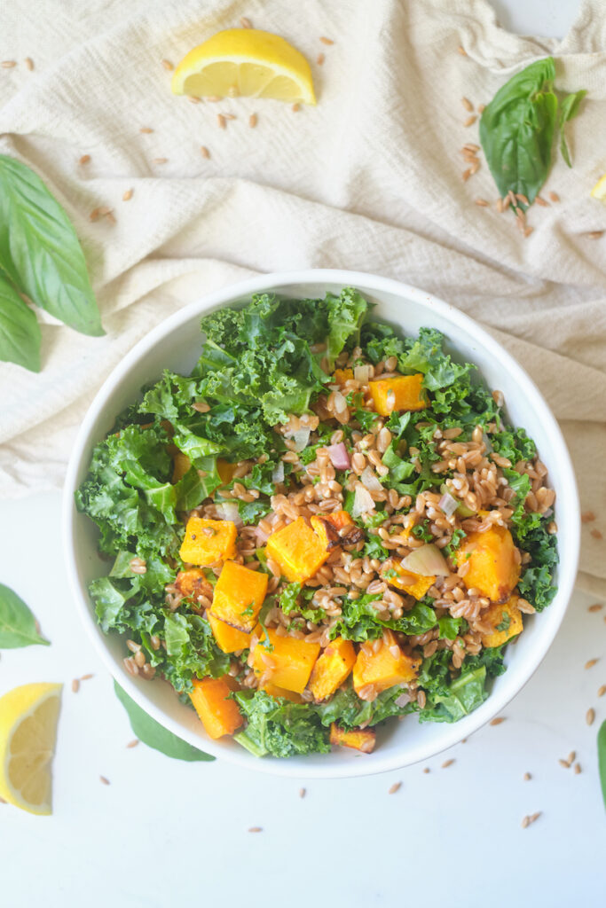 Overhead view of a bowl of farro butternut squash salad with kale and herbs