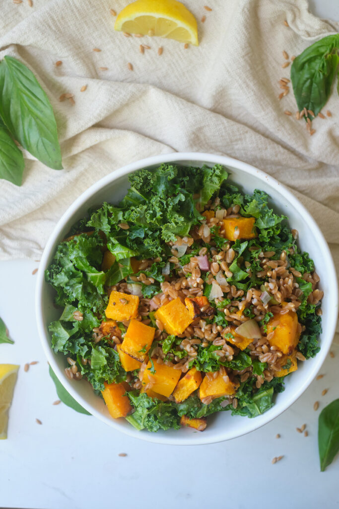 Overhead view of a bowl of farro butternut squash salad with kale and herbs