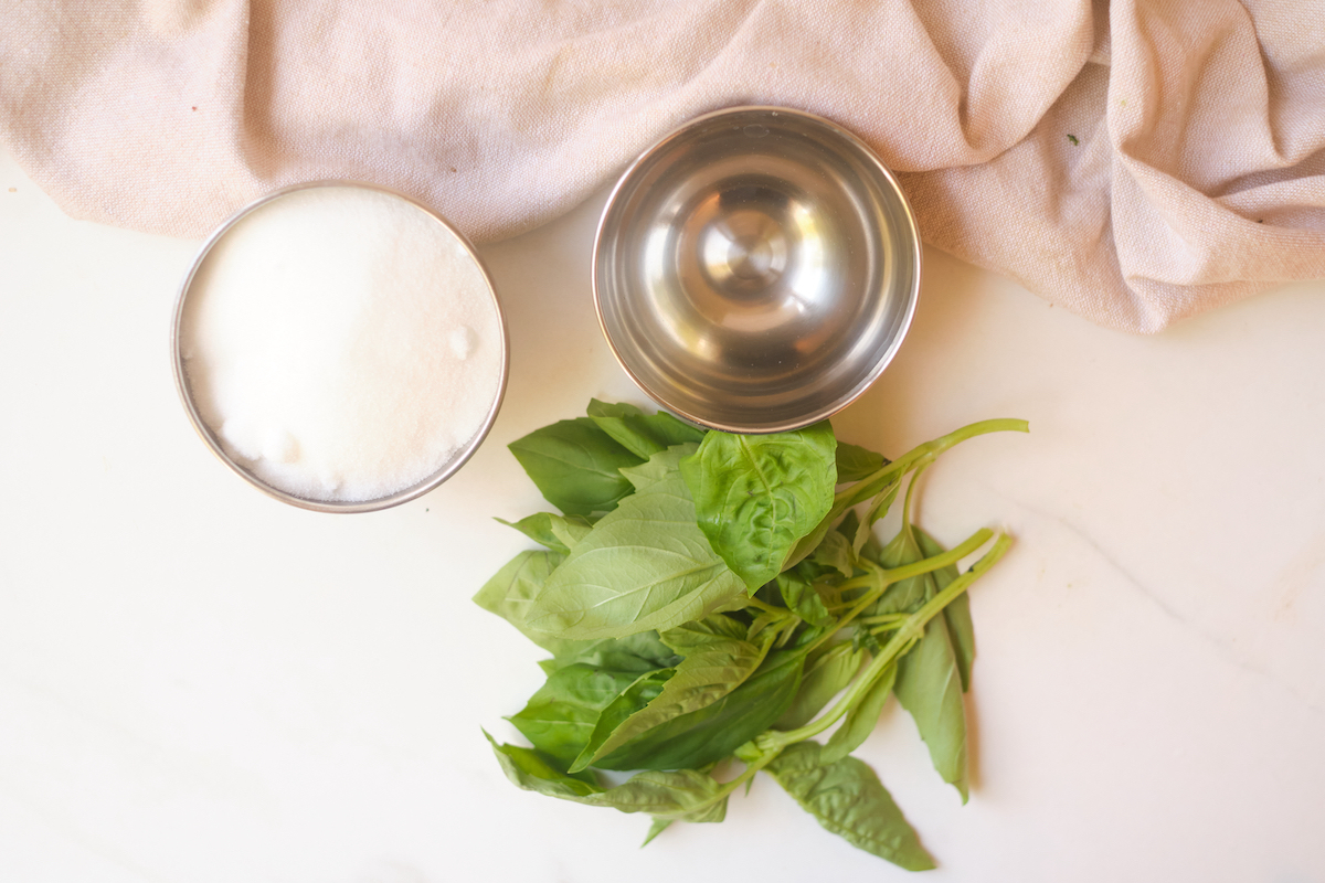 basil leaves, sugar and water on a table show ingredients to make basil simple syrup