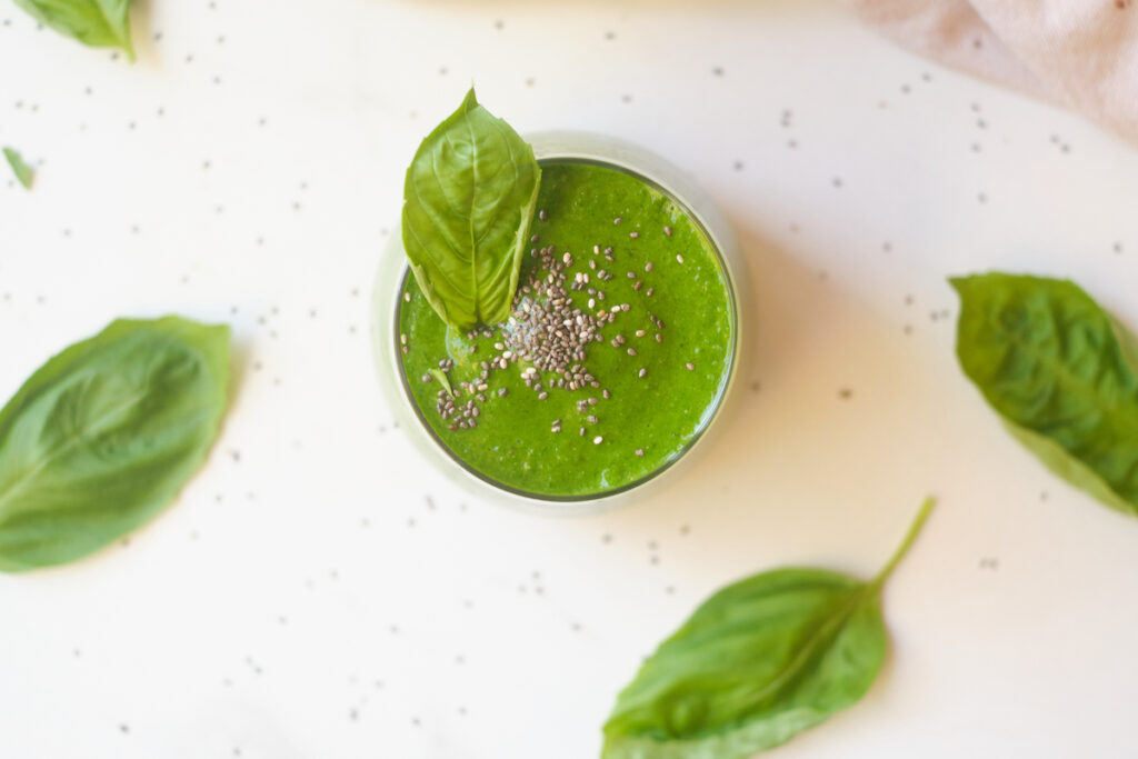birds eye view of a post workout green smoothie in a glass topped with chia seeds and basil leaves