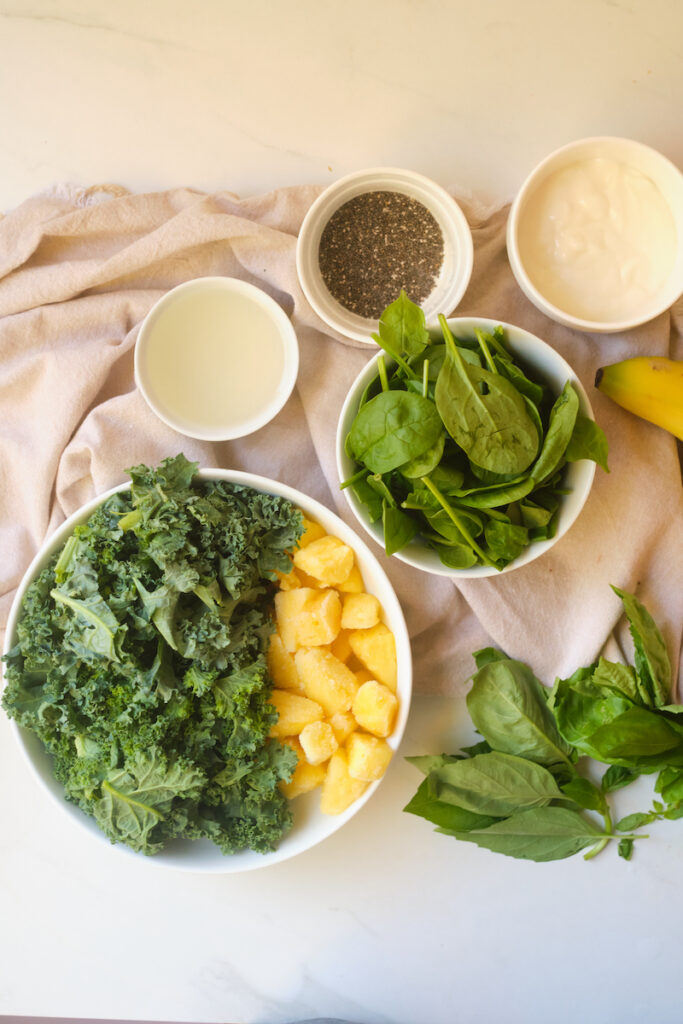 Ingredients for a post workout green smoothie including kale, spinach, pineapple, basil, chia, greek yoghurt, and protein powder