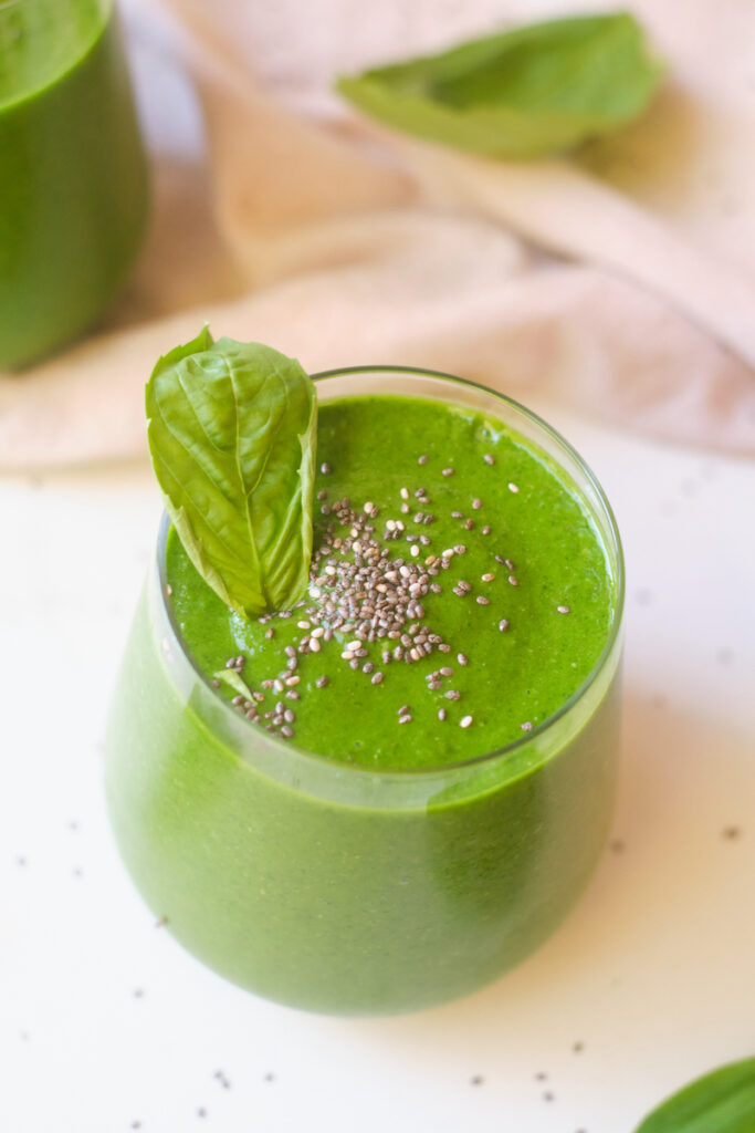 a post workout green smoothie in a glass topped with chia seeds and basil leaf
