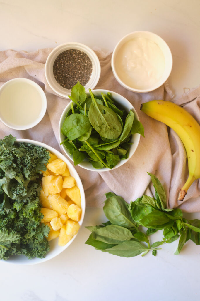 Ingredients for a post workout green smoothie including kale, spinach, pineapple, basil, chia, greek yoghurt, and protein powder