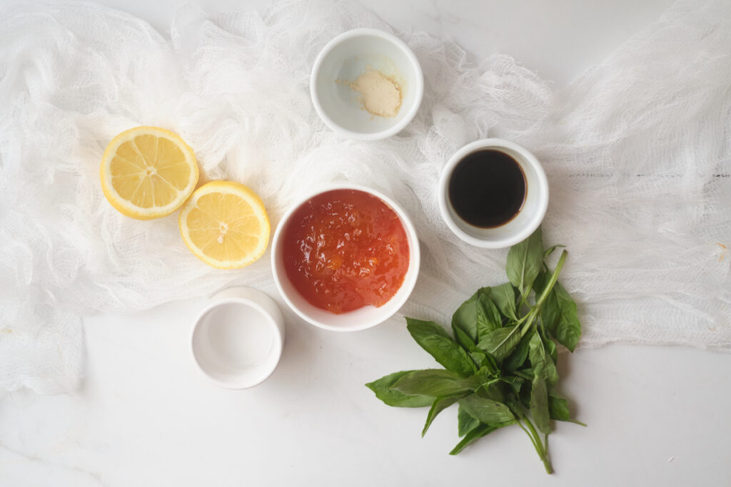 Ingredients for apricot glazed salmon in small dishes on a table, including apricot jam or preserves, soy sauce, basil leaves, and lemon