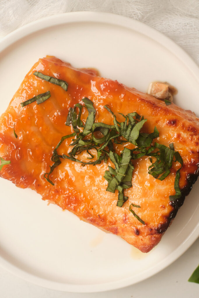 A close up of baked apricot glazed salmon with basil plated on a white plate