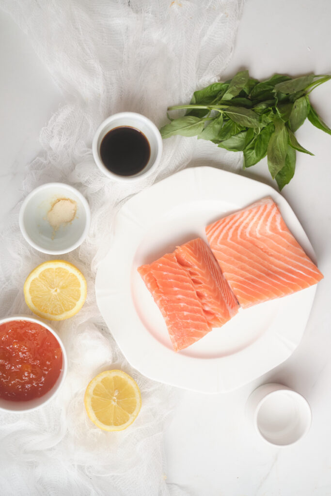 Ingredients for apricot glazed salmon in small dishes on a table, including apricot jam or preserves, soy sauce, basil leaves, and lemon