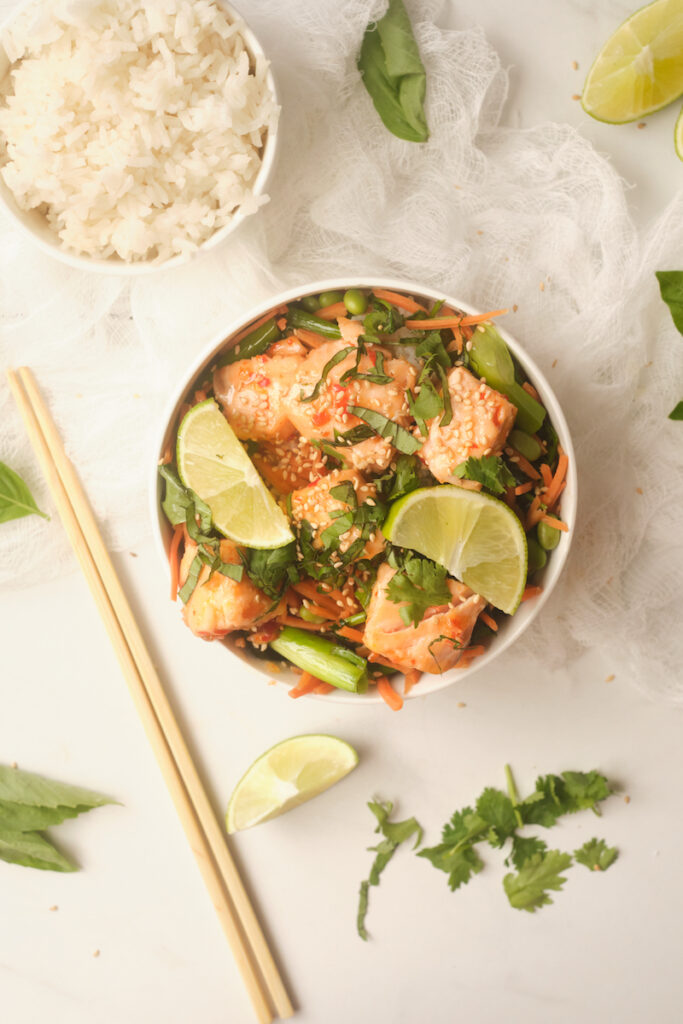 Sweet chilli salmon rice bowls with lime and basil on a table with a bowl of rice and chopsticks