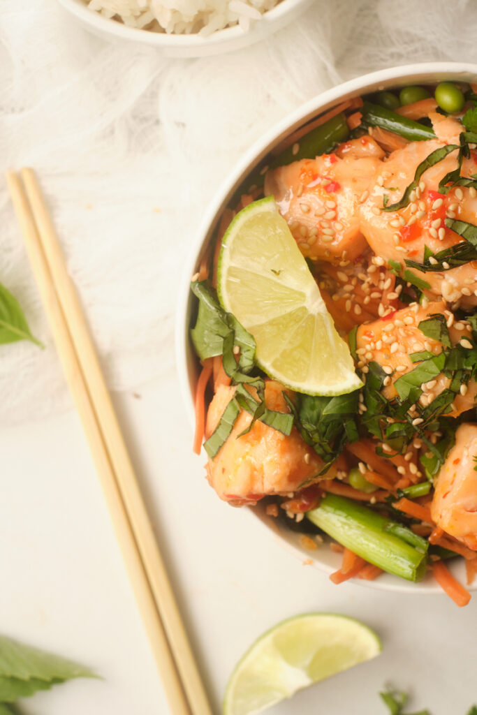 Close up of half a bowl of a sweet chilli salmon rice bowl with lime and basil