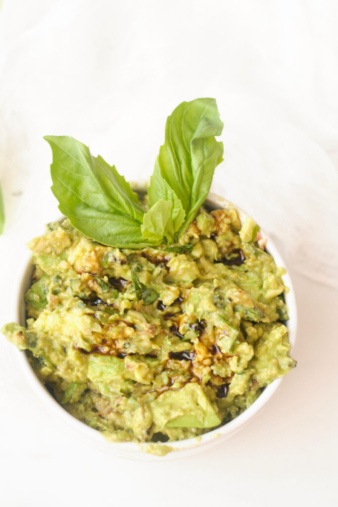 fresh basil guacamole with balsamic reduction in a serving bowl garnished with basil leaves