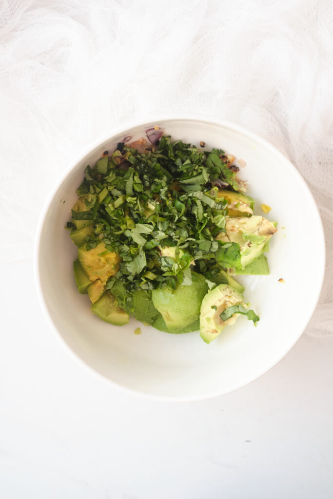 rough chopped basil and avocado cubes in a bowl in preparation to make basil guacamole