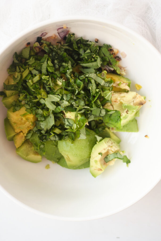 rough chopped basil and avocado cubes in a bowl in preparation to make basil guacamole