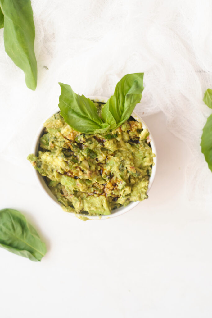 fresh basil guacamole with balsamic reduction in a serving bowl garnished with basil leaves