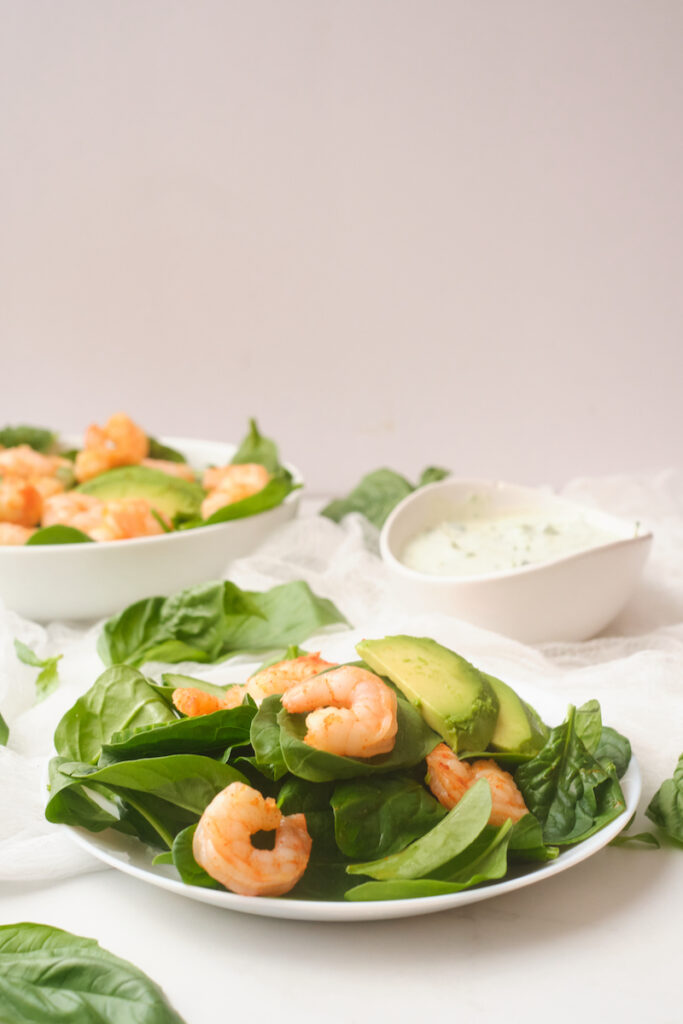 A plate of fresh chilli shrimp and avocado salad with basil green goddess dressing in the background