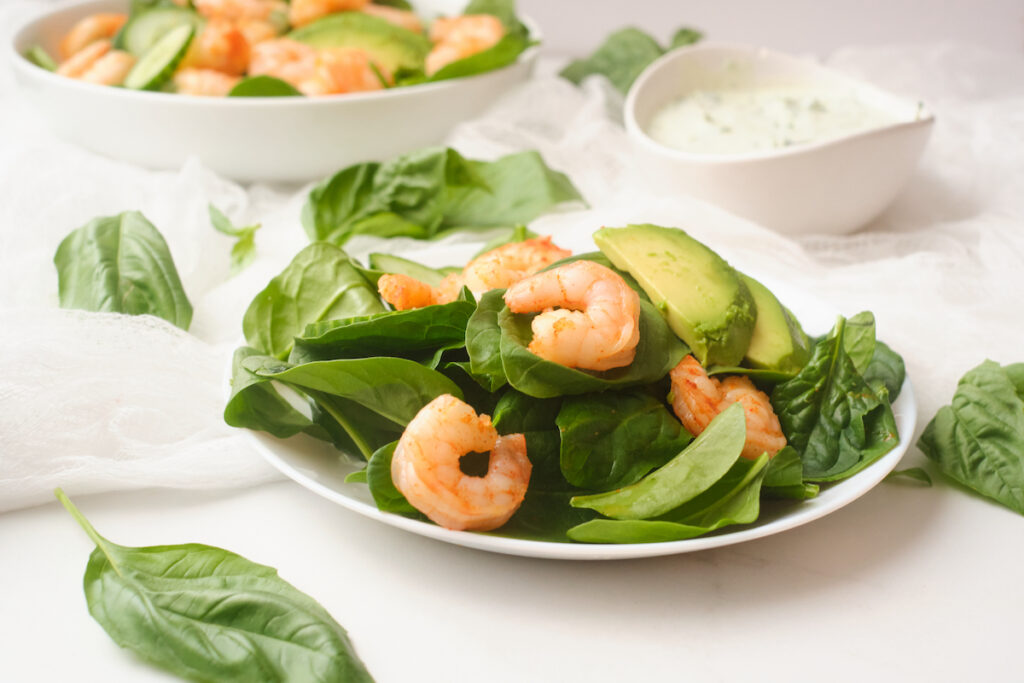A plate of fresh chilli shrimp and avocado salad with basil green goddess dressing in the background