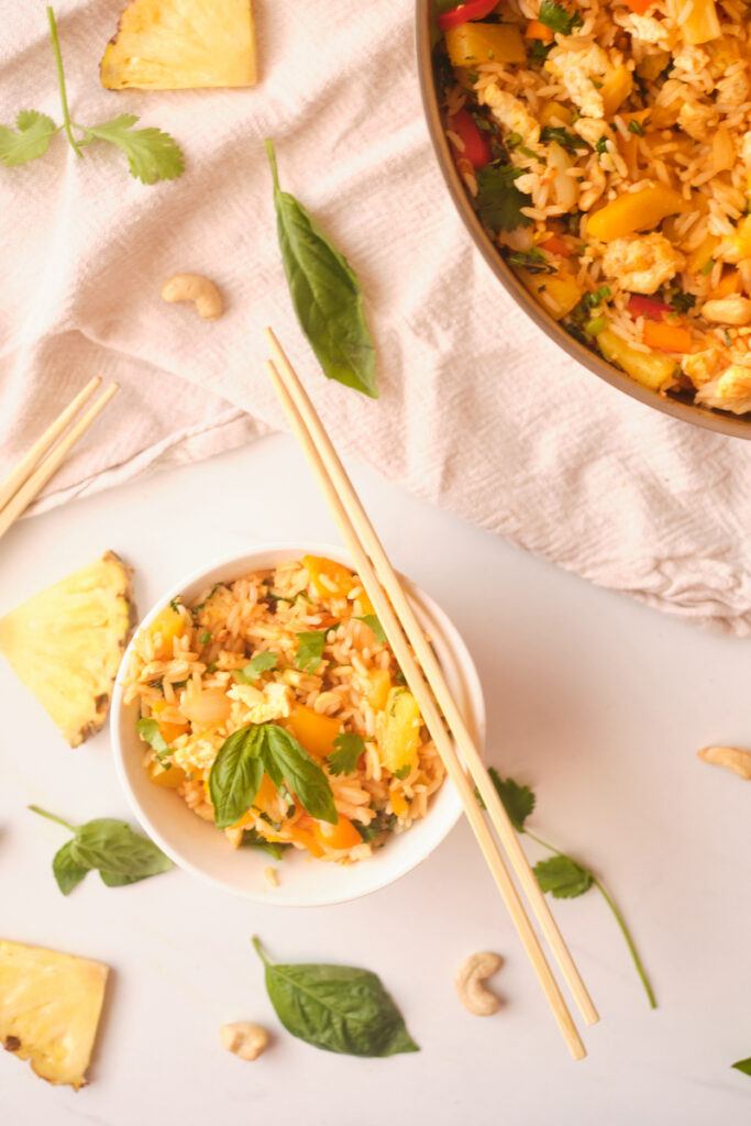 Chopsticks rest on a bowl of thai pineapple fried rice with basil