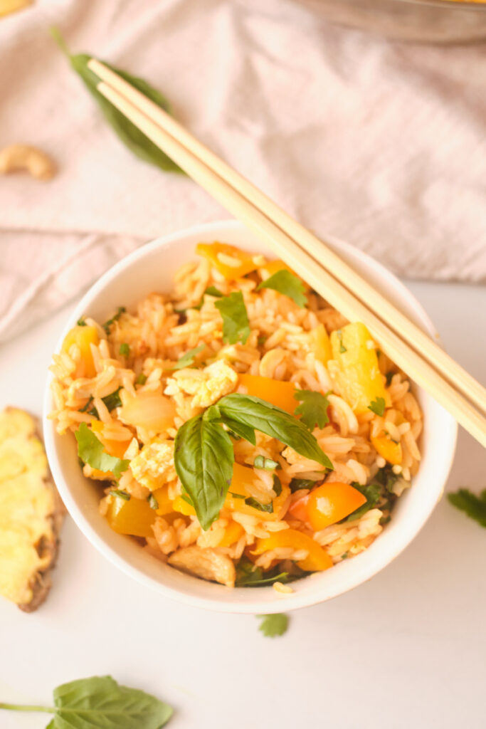 Chopsticks rest on a bowl of thai pineapple fried rice with basil
