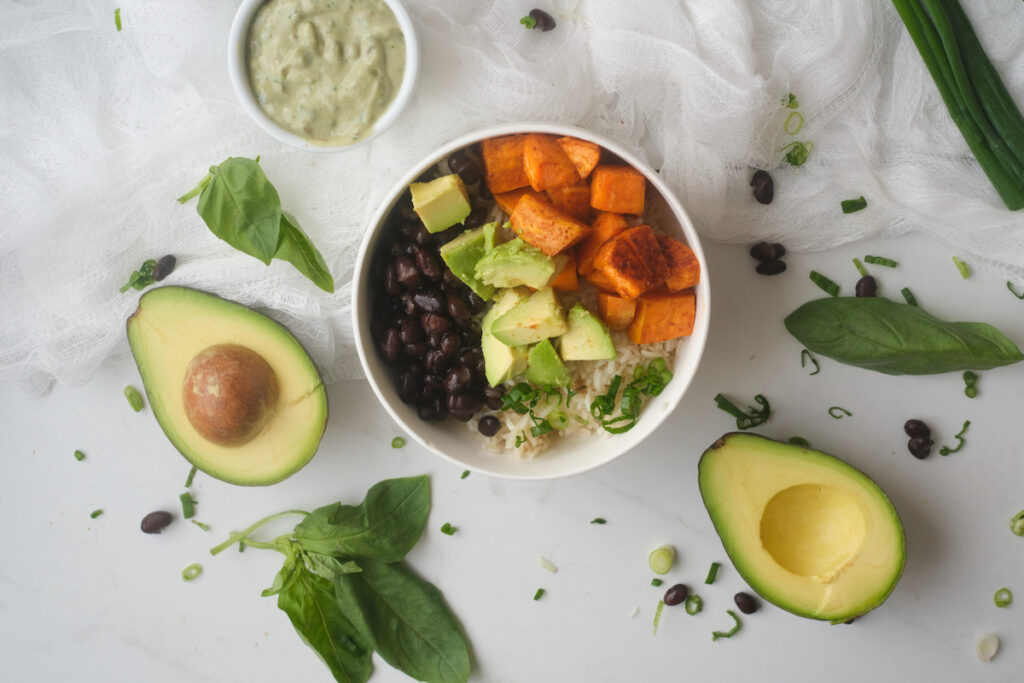 Avocado Sweet Potato Buddha Bowl surrounded by basil yoghurt dressing and basil