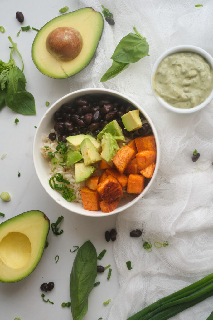 Avocado Sweet Potato Buddha Bowl surrounded by basil yoghurt dressing and basil