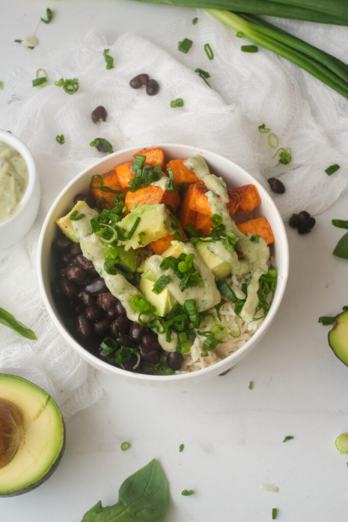 Avocado Sweet Potato Buddha Bowl surrounded by basil yoghurt dressing and basil