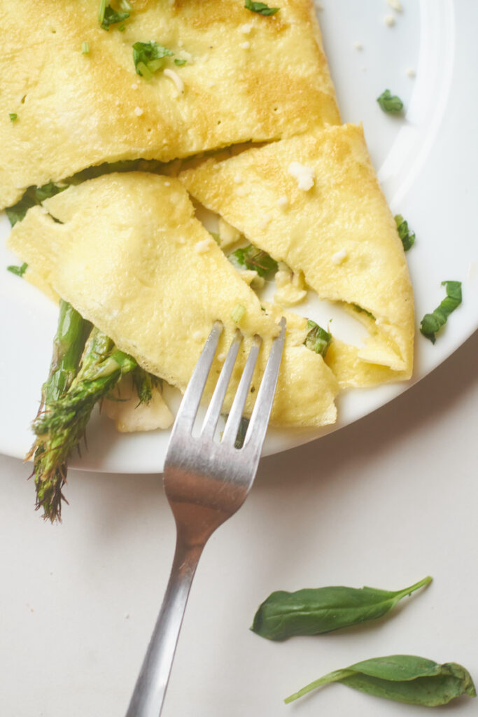 A fork digs into an asparagus omelet with goat cheese and basil on a plate