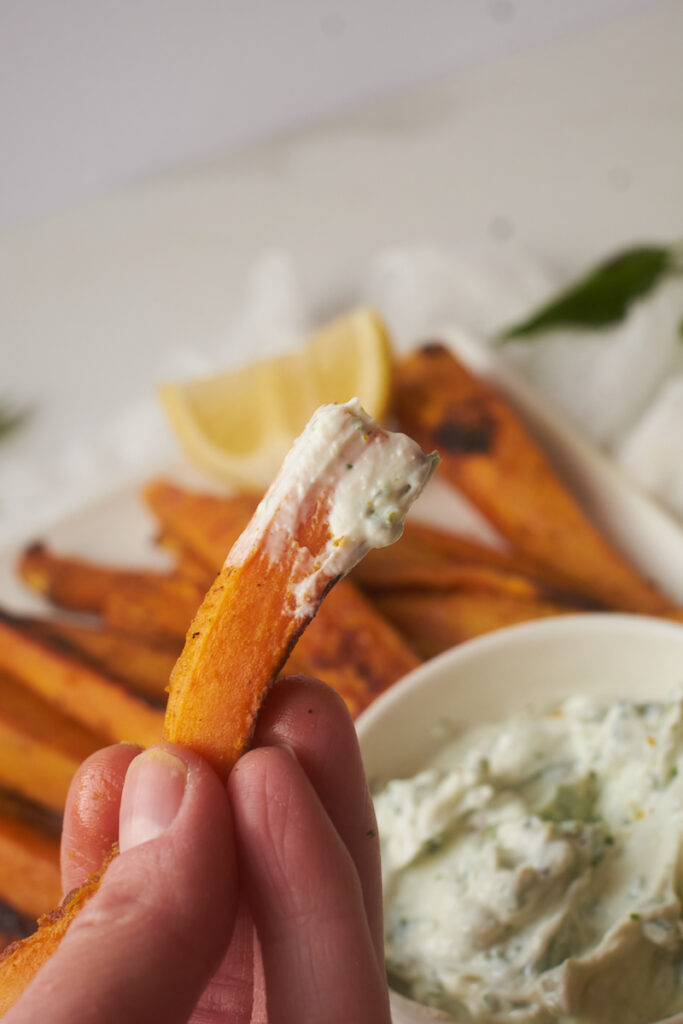 A hand holds a curry yam fry dipped in a basil mint dip