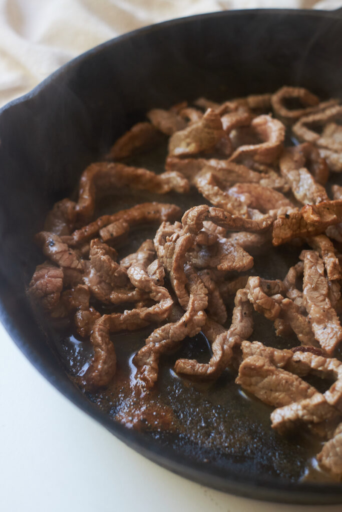 beef strips sizzling in a cast iron pan