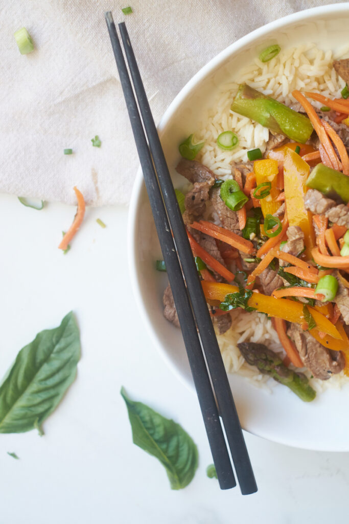 honey ginger beef and basil stirfry served over rice with chopsticks resting on the bowl