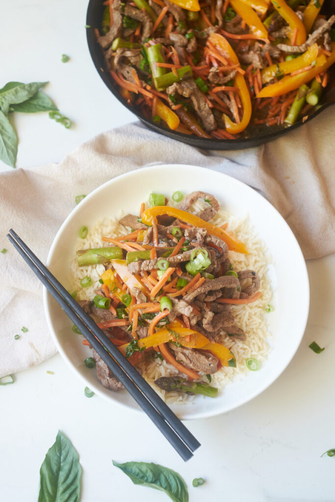 honey ginger beef and basil stirfry served over rice with chopsticks resting on the bowl