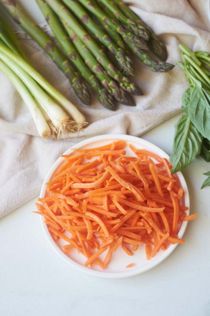 julienned carrots in a dish with asparagus, green onions and basil in view