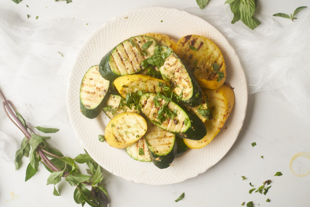 grilled summer squash and zucchini basil recipe served on a plate with thai basil arranged around it