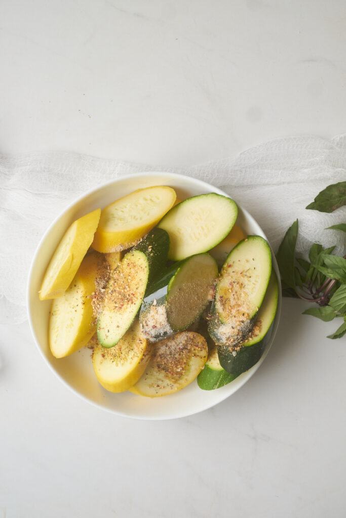 sliced zucchini and summer squash in a bowl with seasoning