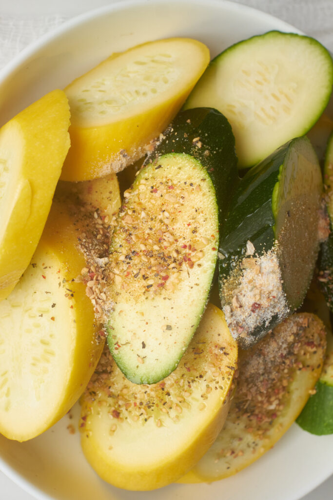 close up of sliced zucchini and summer squash in a bowl with seasoning