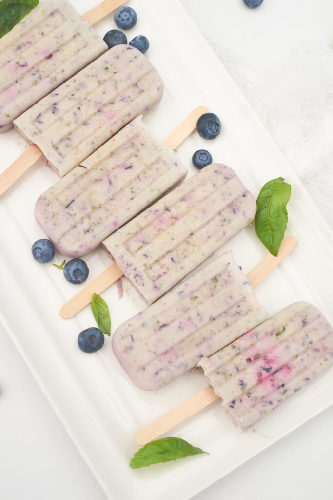 refreshing coconut milk popsicles flavored with basil, blueberry and pomegranate on a plate