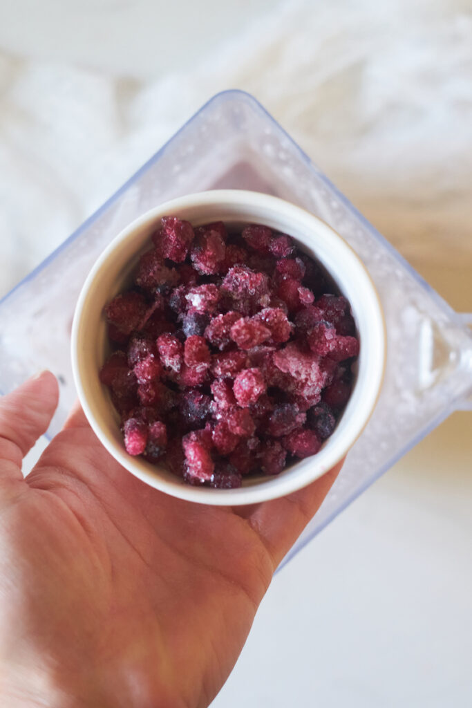 frozen pomegranate arals in a bowl held over a blender before adding