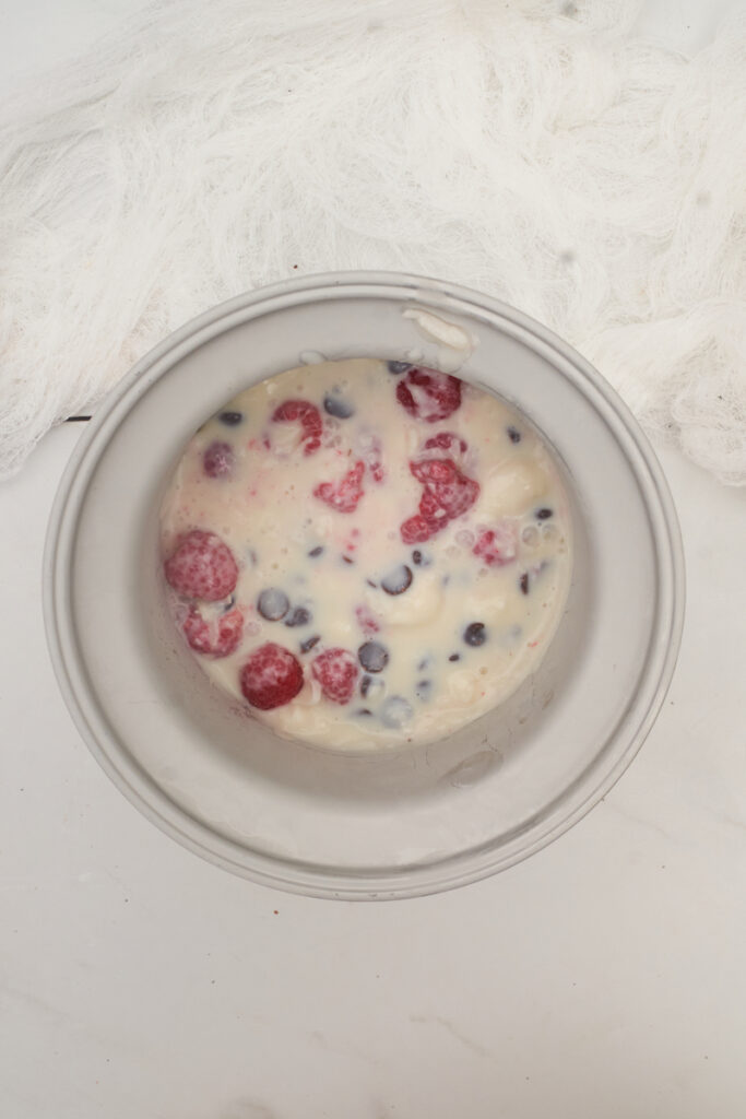 Process shot showing how to make raspberry dark chocolate ice cream with basil using coconut milk instead of dairy. Ingredients in an ice cream maker freezing