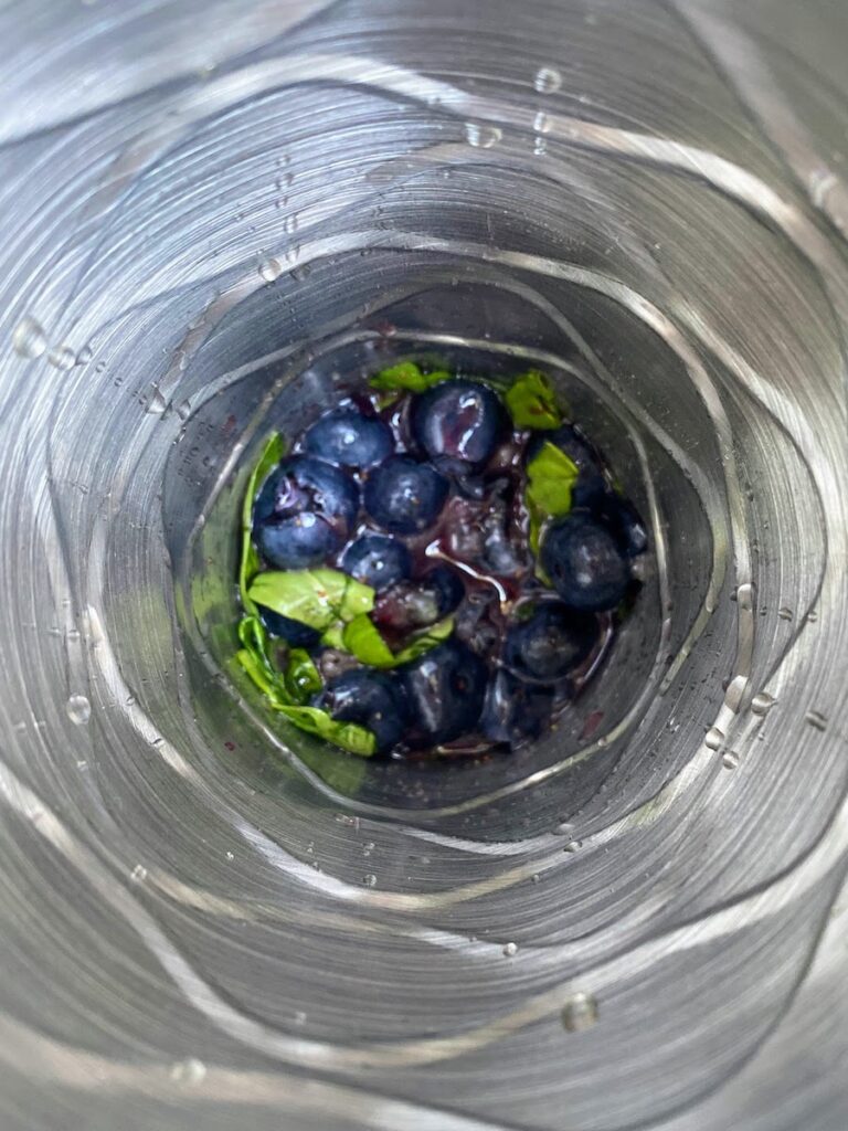 Birdseye view looking down a cocktail shaker at blueberries and basil ready to muddle