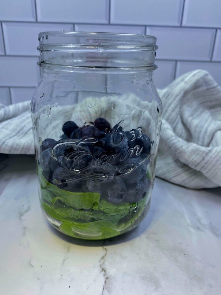 fresh blueberries and basil leaves in a mason jar before vodka is added to make homemade basil blueberry infused vodka