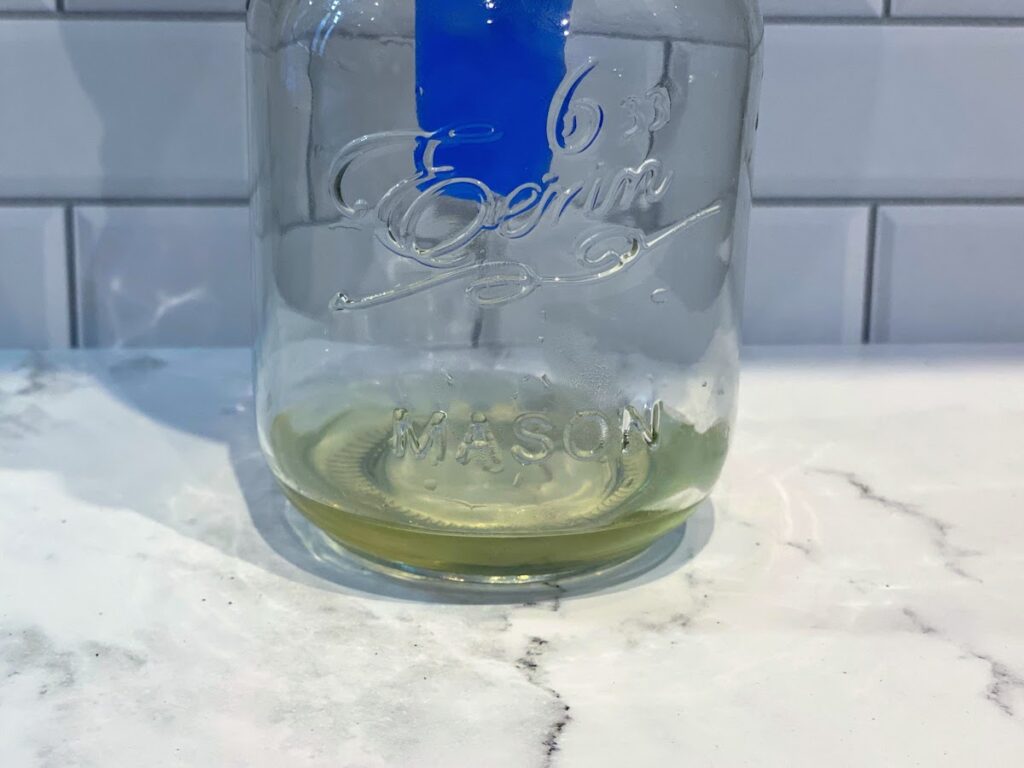 A greenish yellow tinged liquid (blueberry and basil infused vodka) drips from a funnel into a mason jar