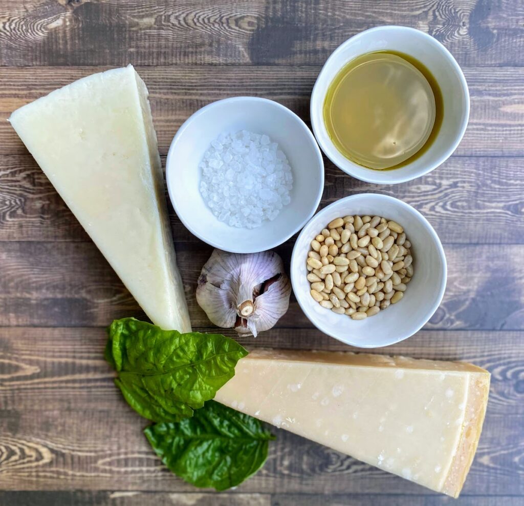 ingredients for tuscany basil pesto including pecorino cheese, parmesan cheese, course salt, garlic, pine nuts, olive oil, and tuscany basil